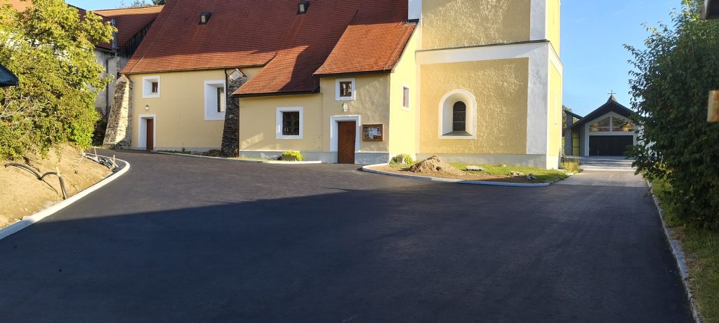 Neuer Asphaltweg vor einem gelben Kirchengebäude mit rotem Ziegeldach in Österreich