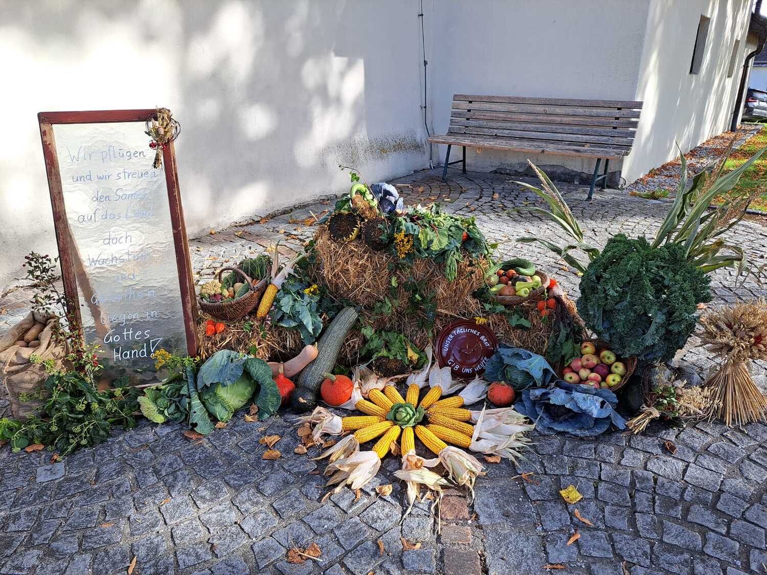 Erntedankdekoration mit Gemüse, Mais und Stroh vor weißer Wand